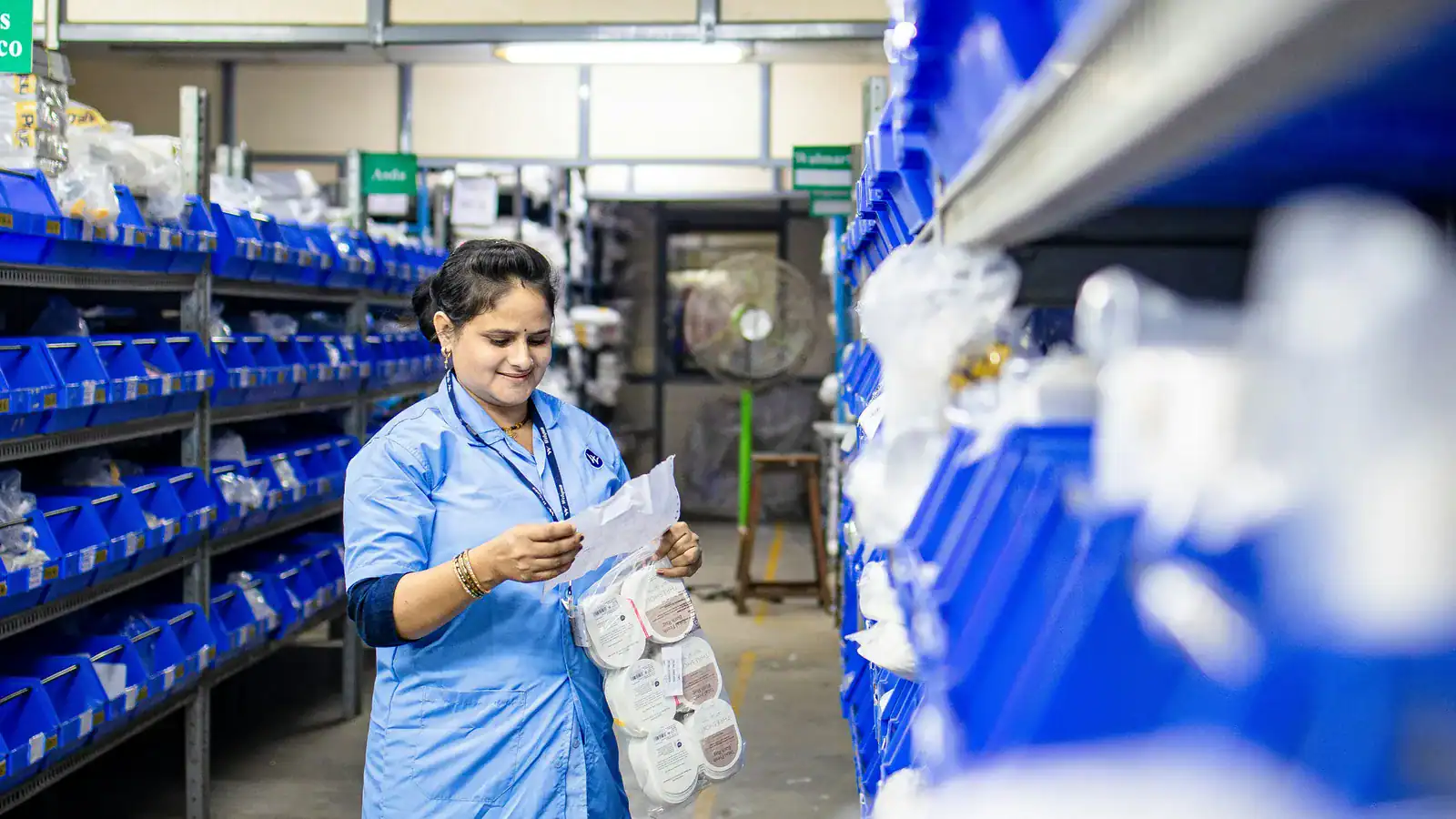 Warehouse worker checking parts against a list beside blue storage bins