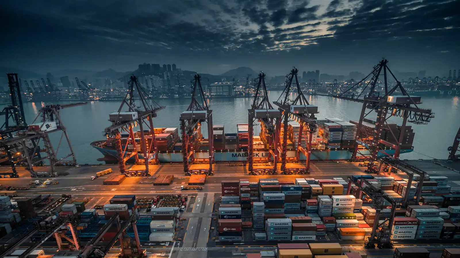 Container ship being loaded by cranes at an industrial port at dusk