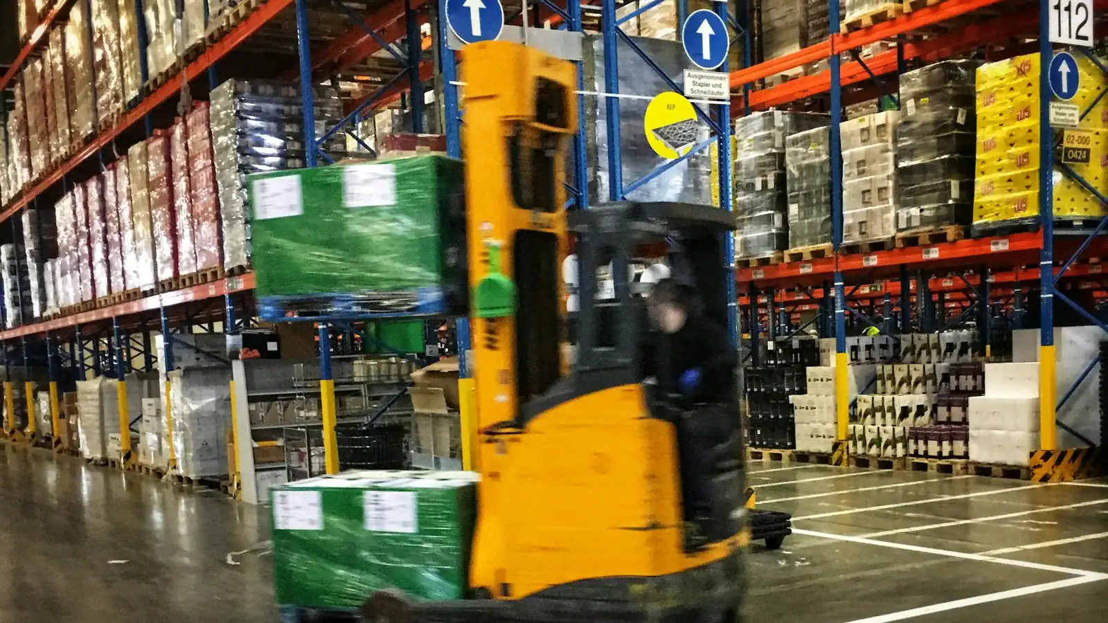 Reach truck moving a pallet through a high-bay warehouse aisle